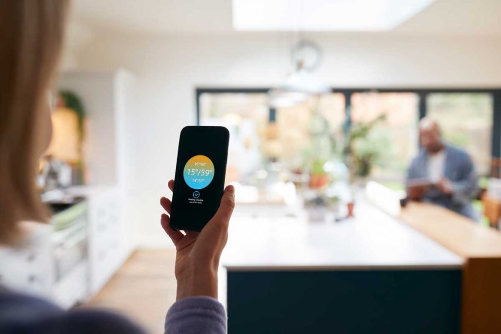 Mature Woman Using App On Phone To Control Digital Best Smart Thermostats For Heat Pumps